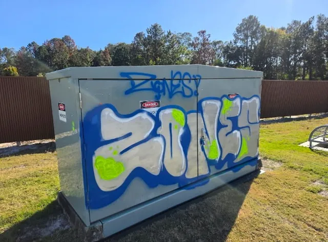 Before graffiti removal: blue, silver and green graffiti on a metal utility cabinet in Kingscliff